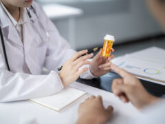 Doctor holding medicine bottle and pen, explaining prescription to patient
